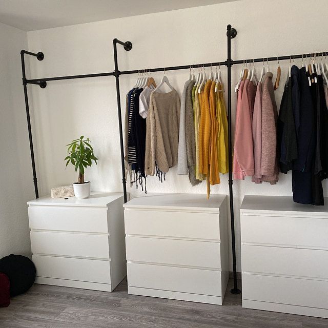 a room with white drawers and clothes hanging on the wall next to a plant in a pot