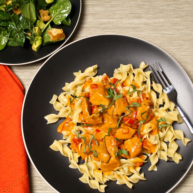 a plate of pasta with chicken and sauce on it next to a bowl of spinach