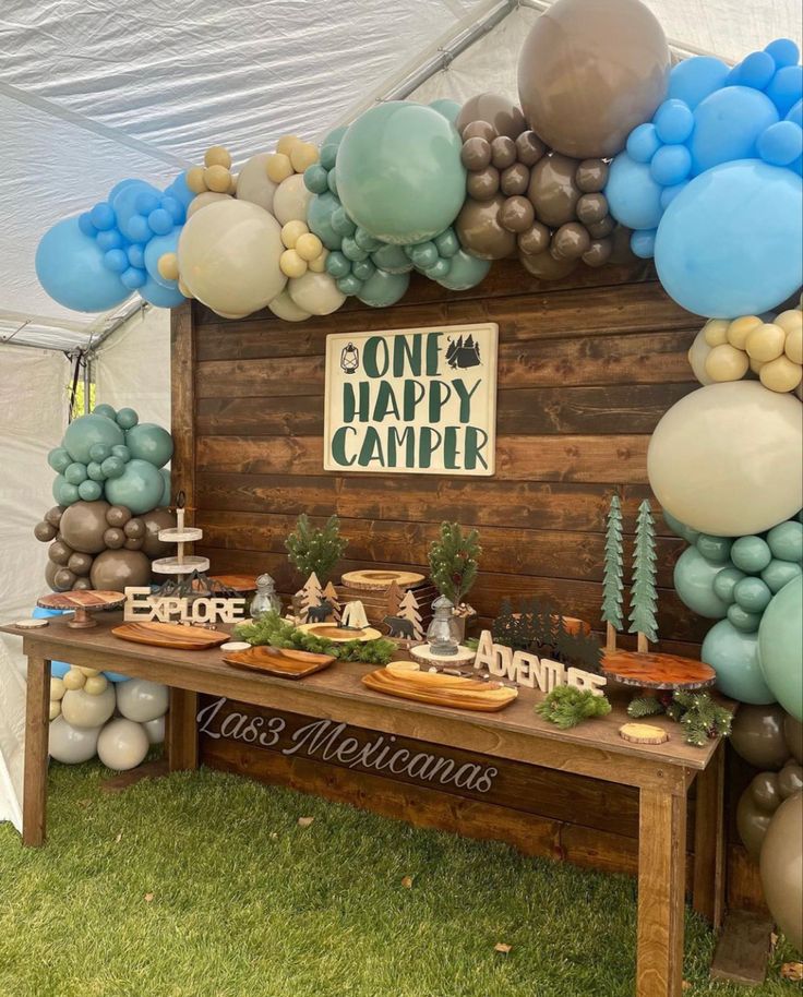 a wooden table topped with lots of balloons next to a sign that says one happy camper