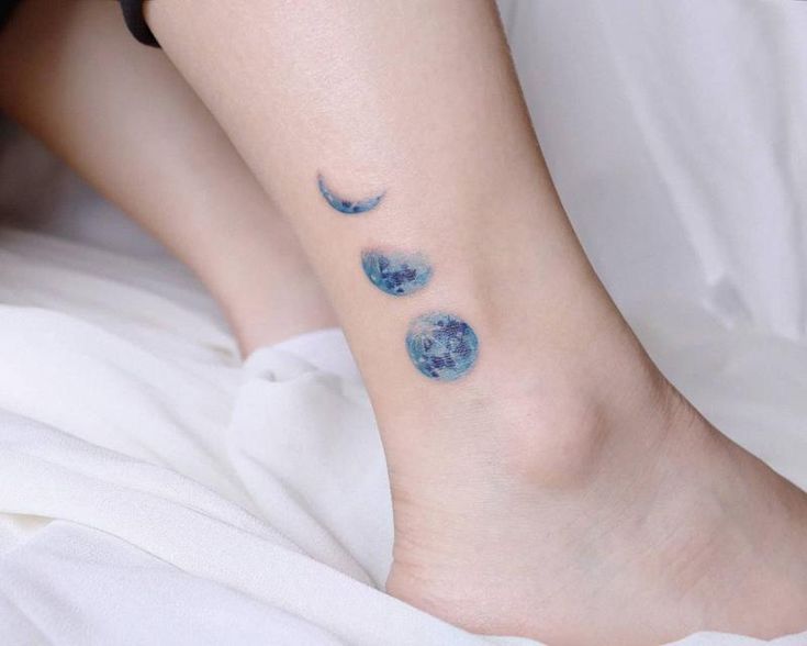 a woman's foot with three blue moon tattoos on it