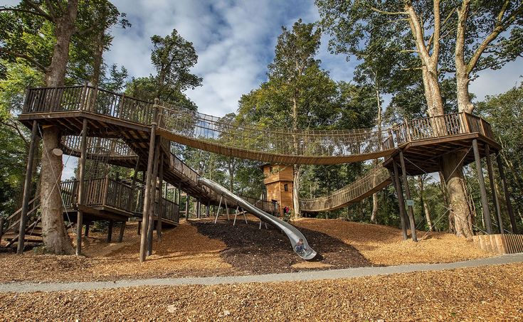 a tree house with a slide in the middle of it and lots of wood chips on the ground