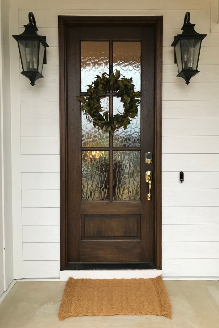 a front door with a wreath on it and two lights hanging from the side wall