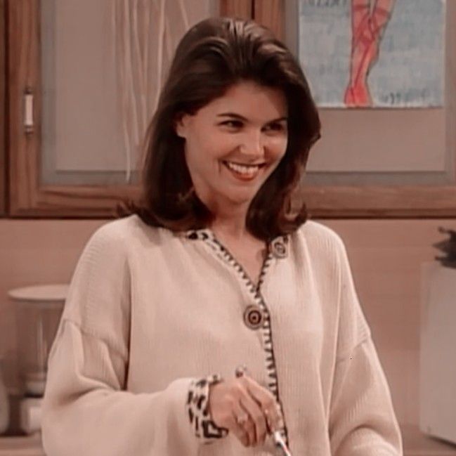 a woman standing in a kitchen holding a knife and smiling at the camera while wearing a sweater