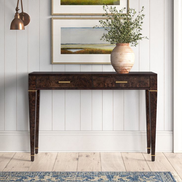 a vase sitting on top of a wooden table next to a wall with pictures above it