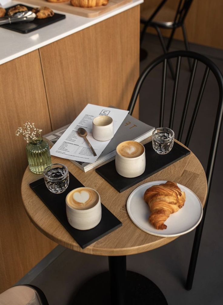 two plates with croissants and coffee are on a small table in front of the counter