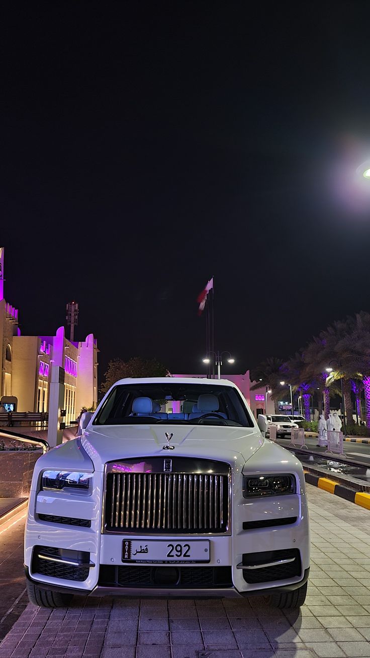 a white rolls royce parked in front of a building at night with purple lights on it