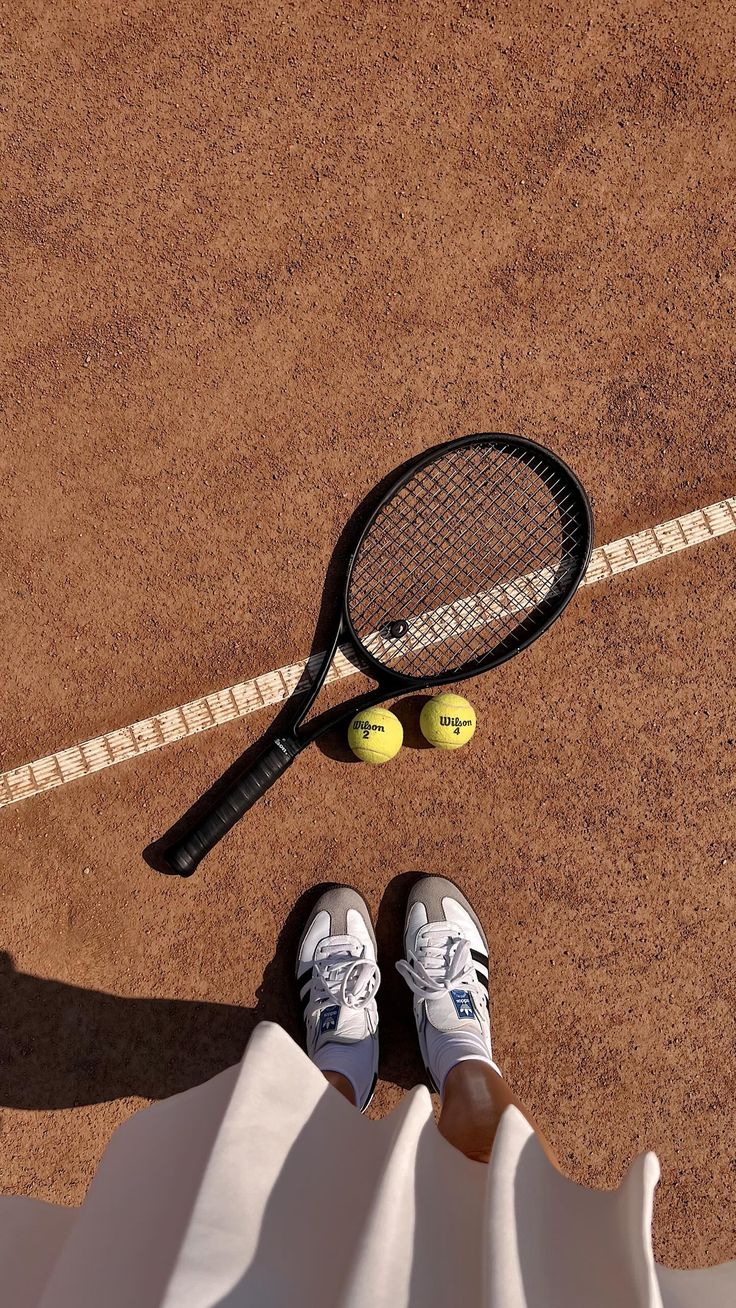 a tennis racket and two tennis balls sitting on the ground next to a person's feet