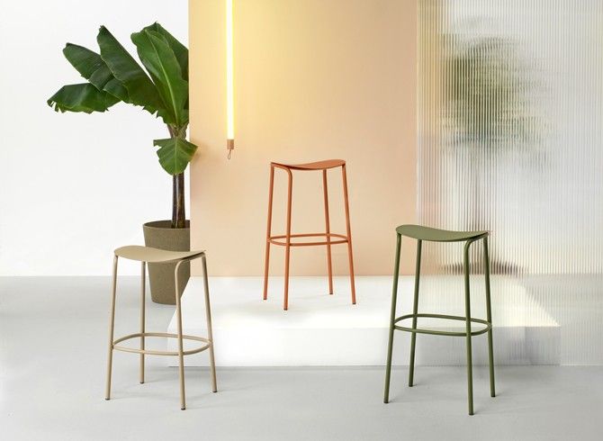 three modern stools and a plant in a room with white walls, one is green and the other is beige