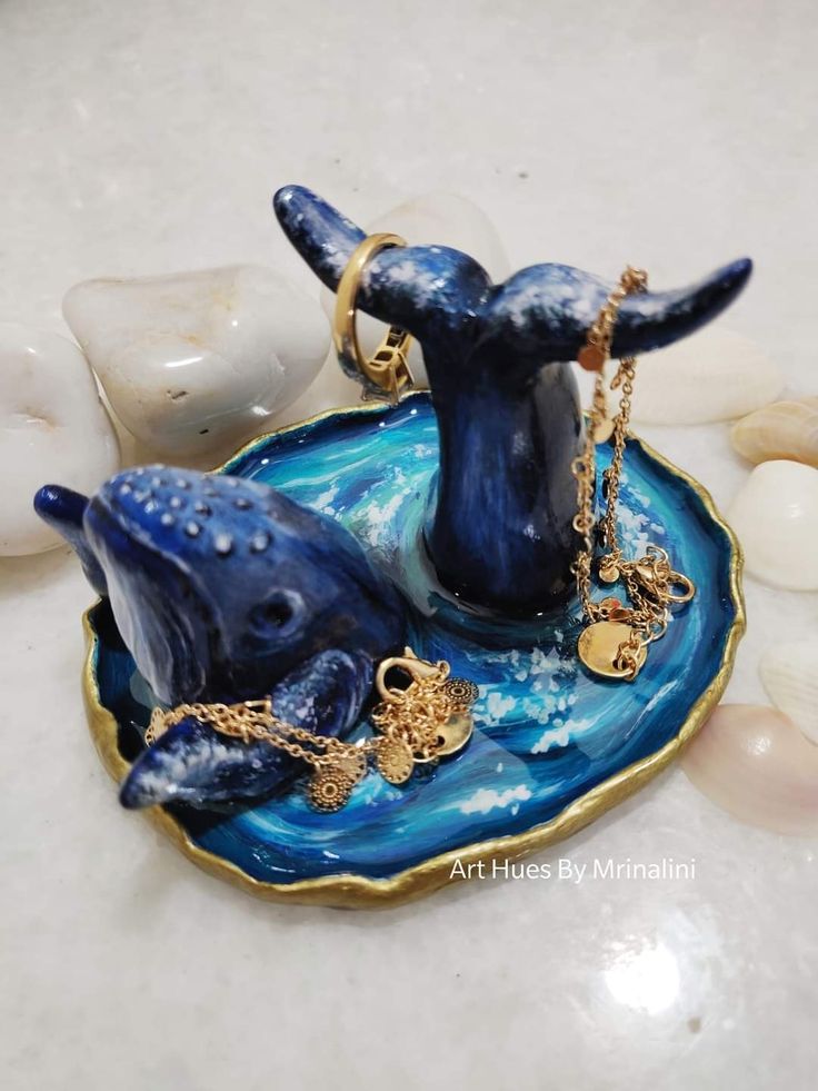 two blue whale figurines sitting on top of a plate with gold chains hanging from it's sides