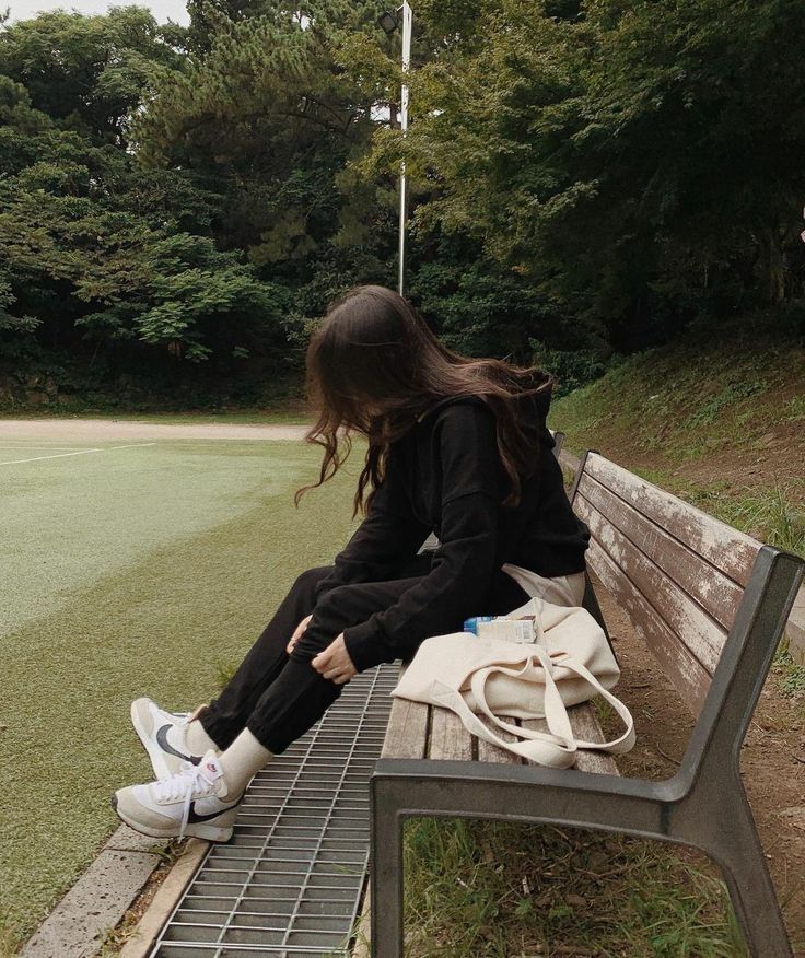 a woman sitting on top of a wooden bench next to a white bag and purse