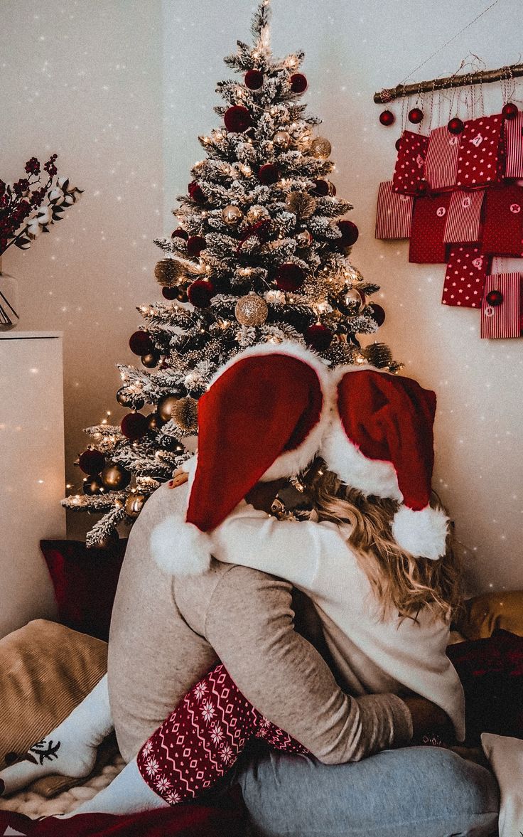 a woman wearing a santa hat sitting in front of a christmas tree