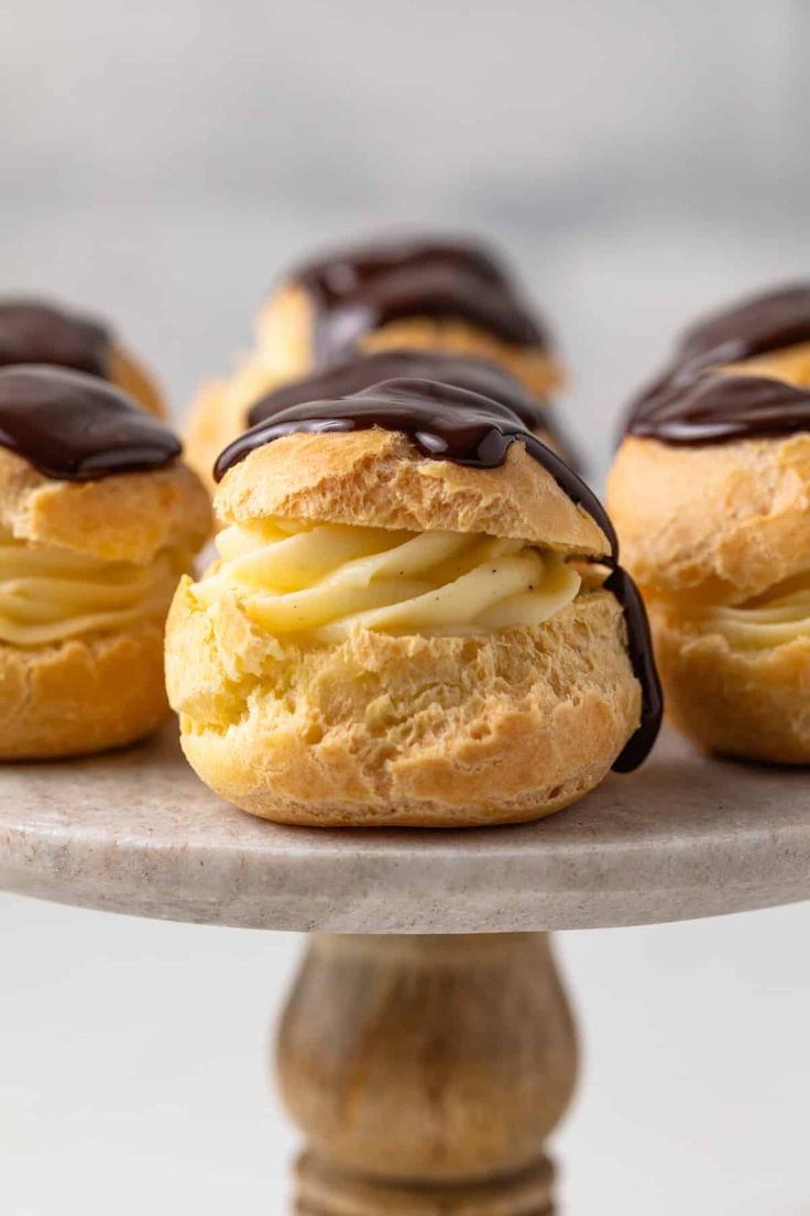 several pastries with chocolate icing sitting on top of a cake plate