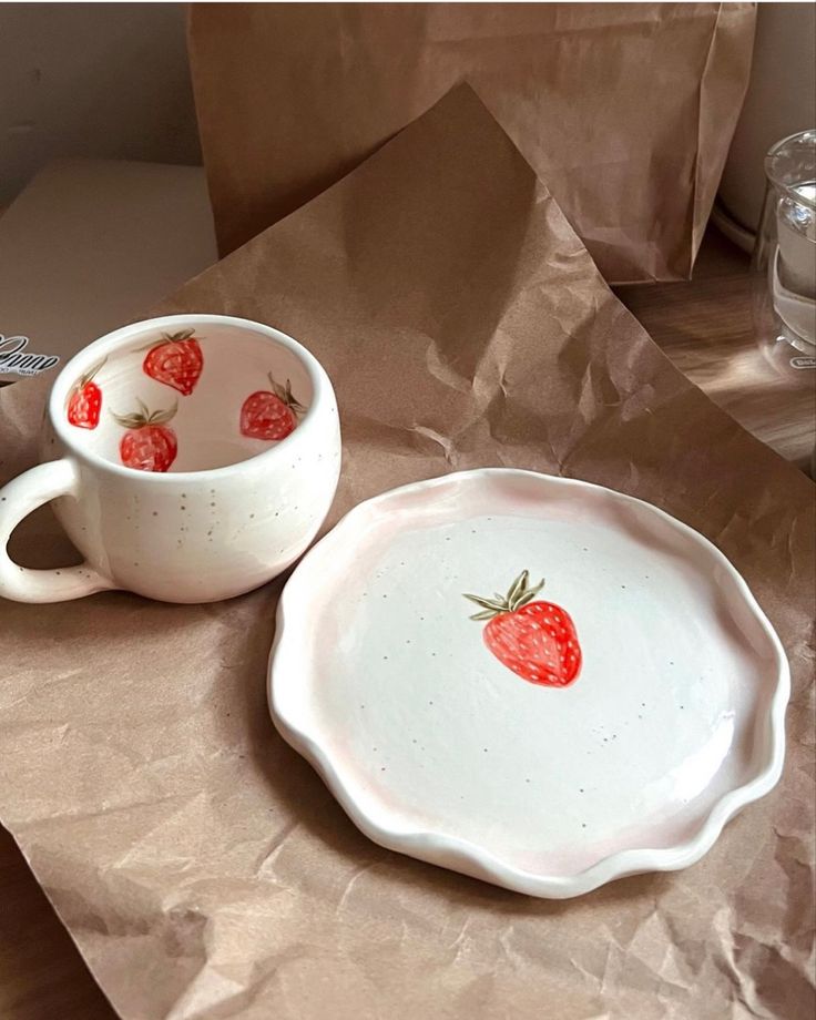 two bowls with strawberries painted on them sitting on a table next to brown paper