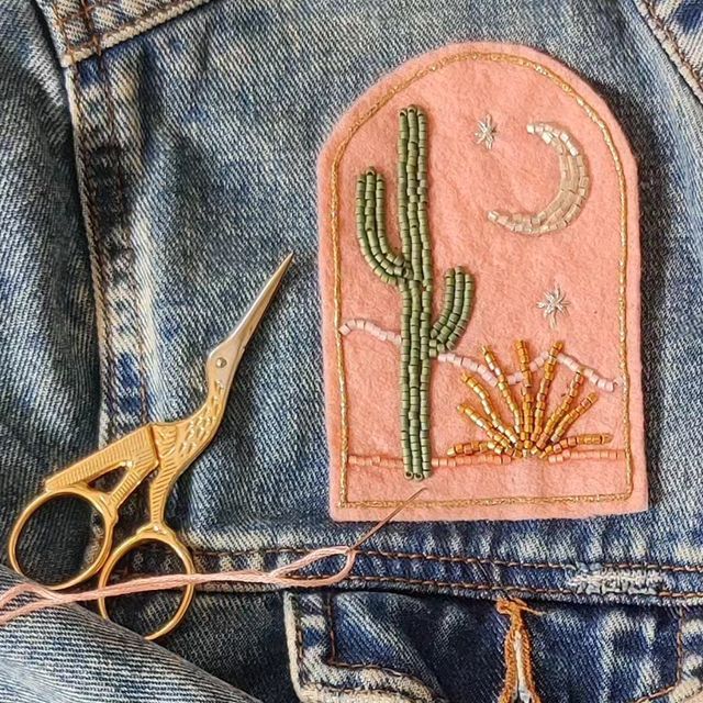 a pair of scissors sitting in the pocket of a jean jacket with embroidered cactus on it