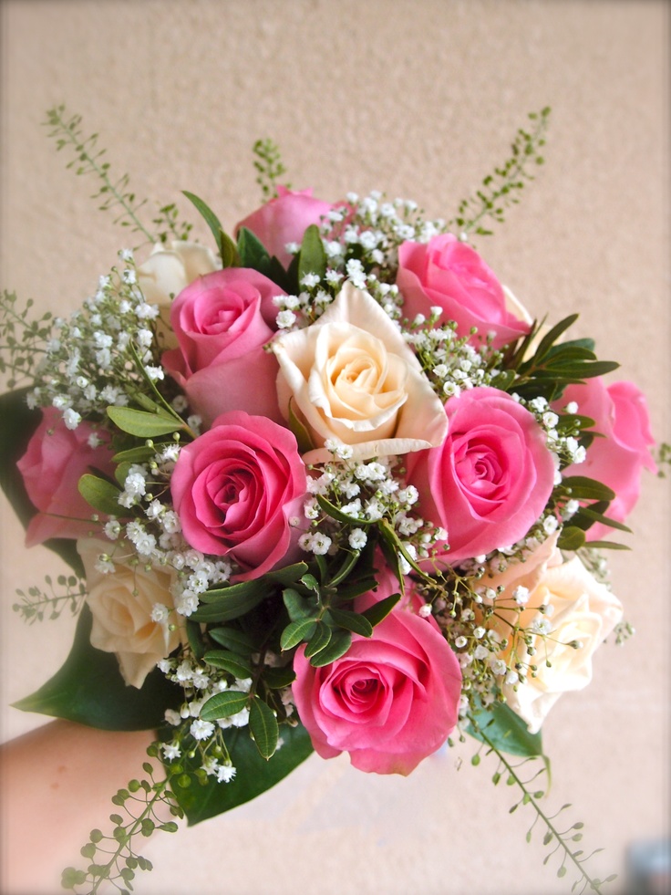 a bouquet of pink and white roses in someone's hand with baby's breath