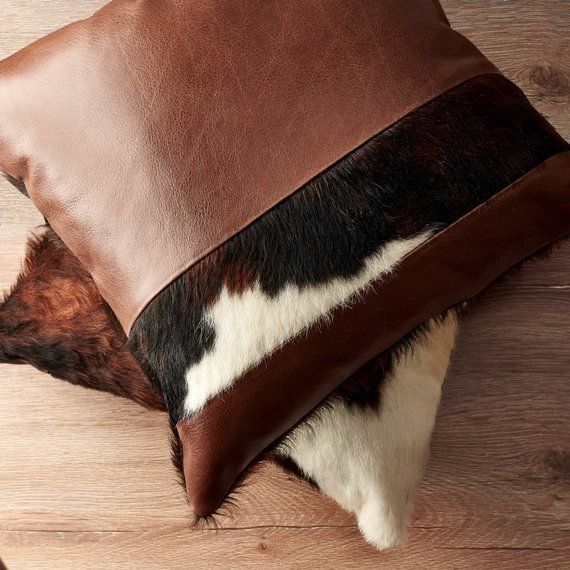 a brown and white cow hide pillow on top of a wooden floor next to a lamp