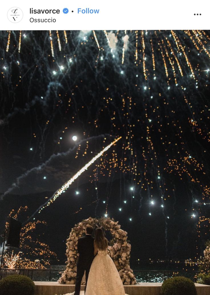 a bride and groom standing in front of fireworks at their wedding ceremony with the night sky behind them