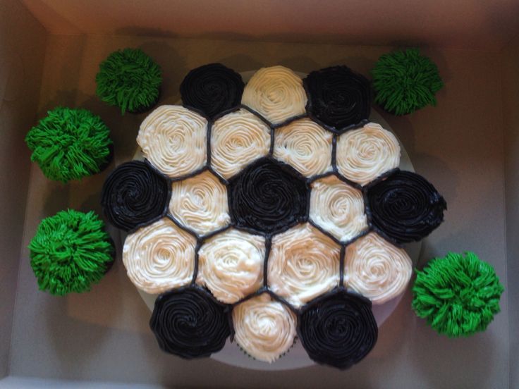 cupcakes with black and white frosting in a box surrounded by green pom - poms