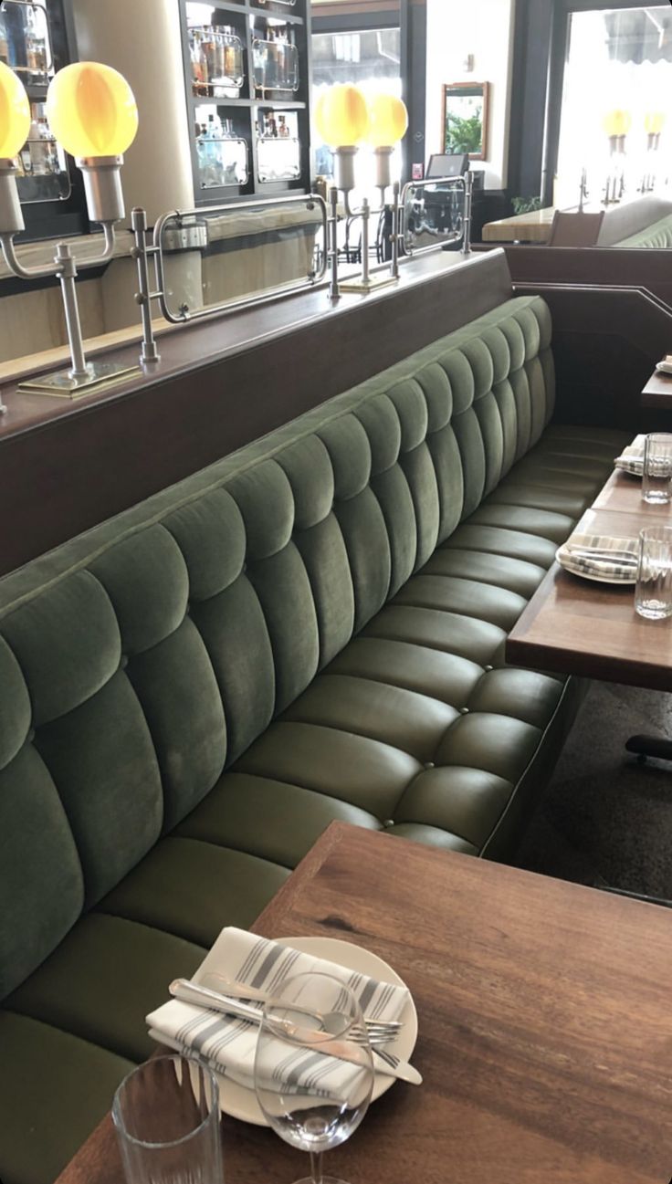 an empty restaurant with green velvet booths and wooden tables, along with glassware on the table