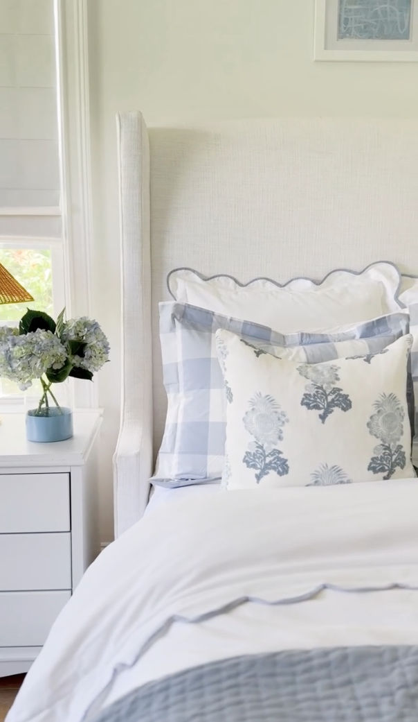 a white bed with blue and white pillows on top of it next to a night stand