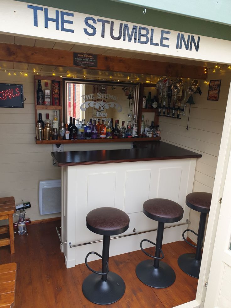 a small bar with three stools in front of it and a sign that says the stumble inn