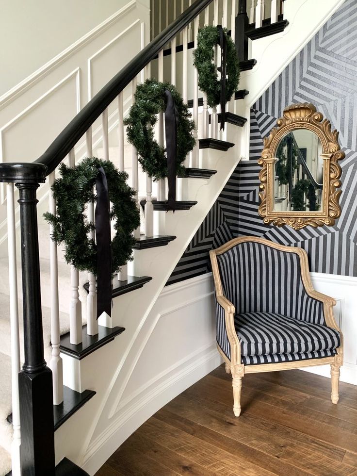 a chair sitting in front of a stair case with wreaths on the banister