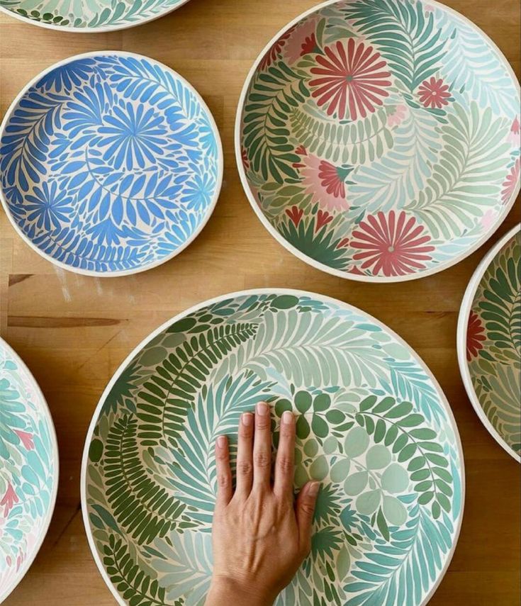 four plates with different designs on them, one being painted by someone's hand