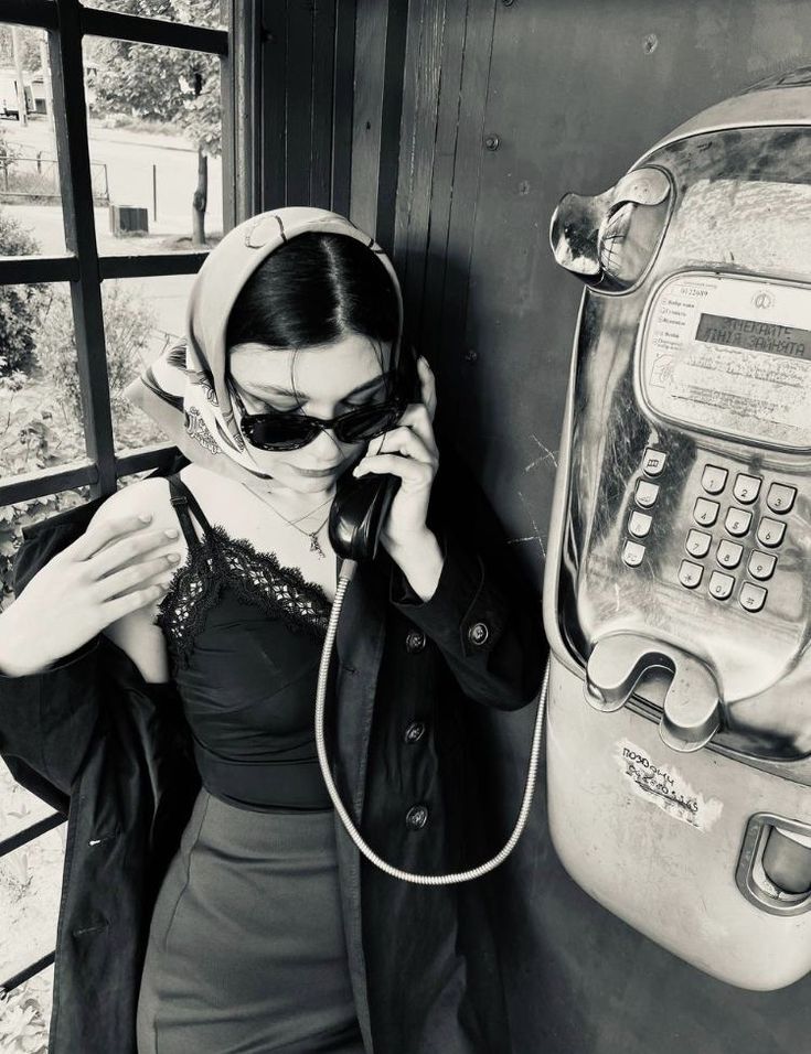 a woman is talking on the phone next to an old payphone