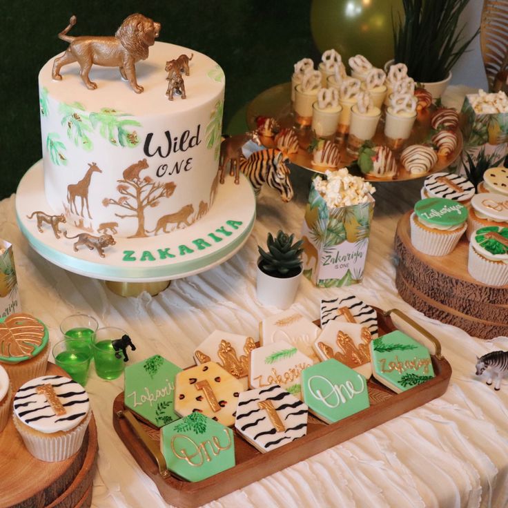 a table topped with cakes and cupcakes covered in animal themed icing next to other desserts