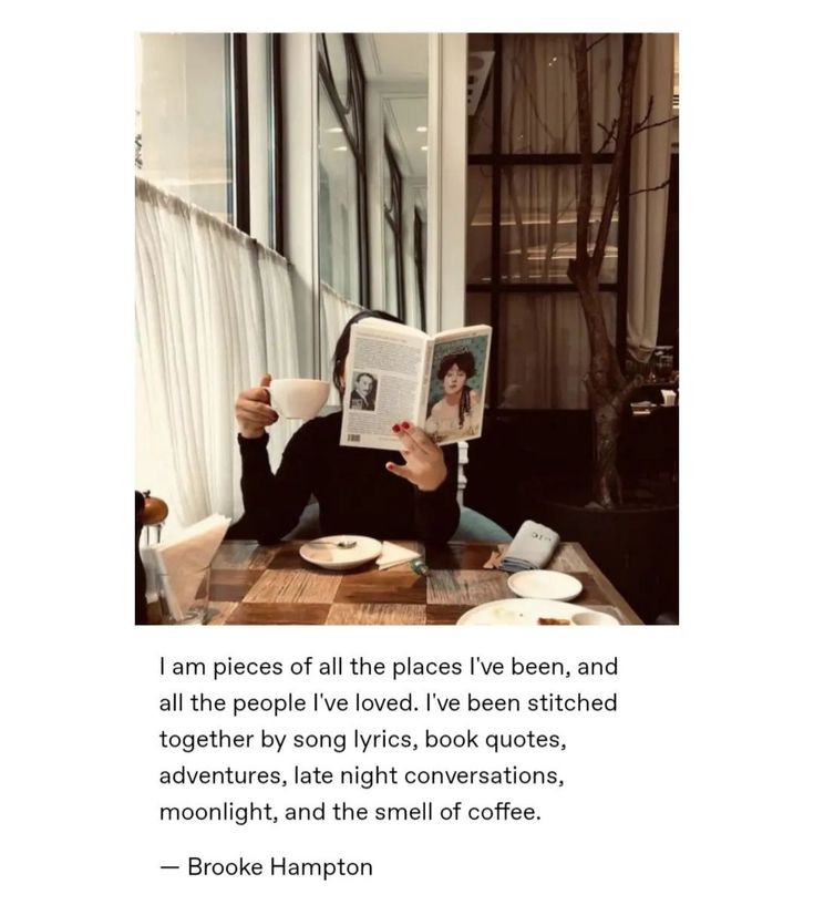 a woman sitting at a table reading a book and holding a coffee mug in her hand