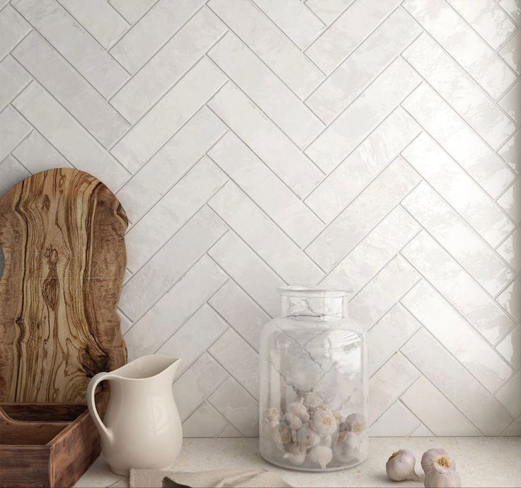 a kitchen counter with white herringbone tile on the wall and wooden cutting board next to it