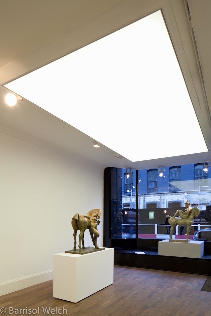 two sculptures on pedestals in front of a window with an open skylight above them