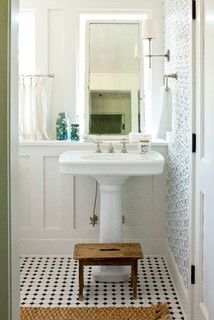 a white sink sitting under a bathroom mirror next to a wooden foot stool in front of a window