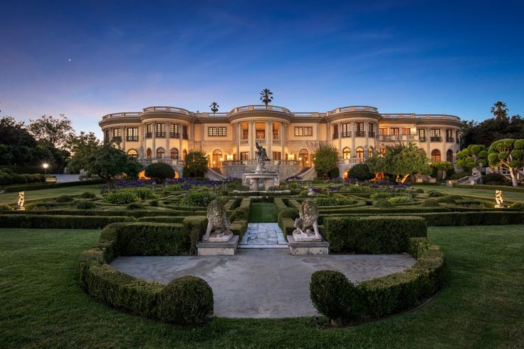 a large mansion with hedges in front of it at night, surrounded by trees and bushes