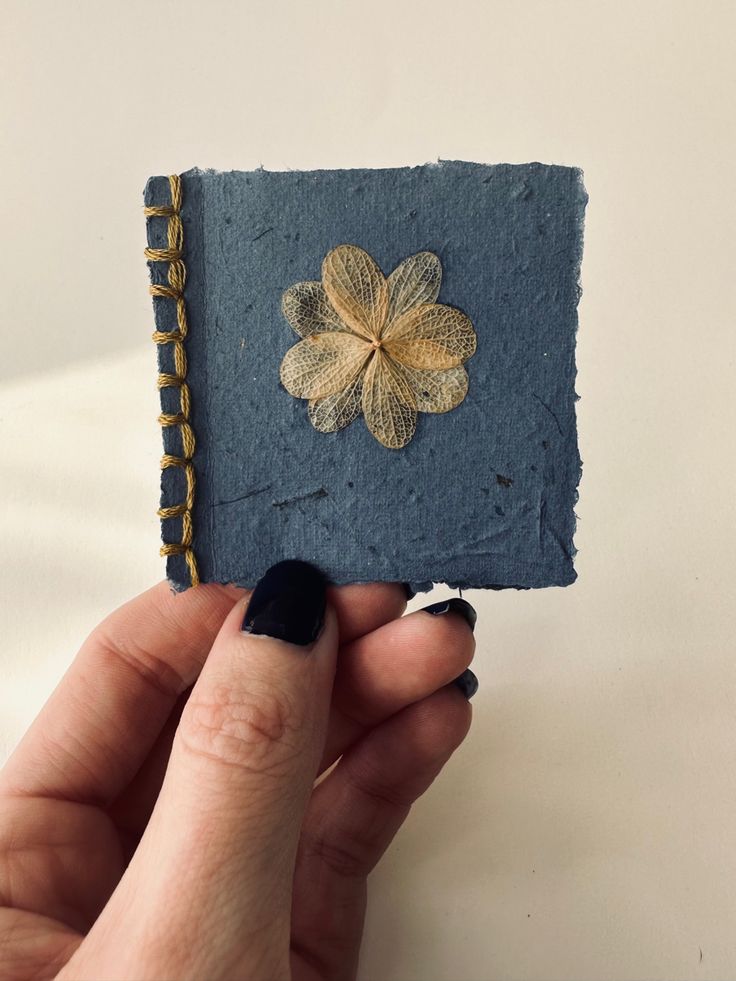 a person holding up a small book with a flower on it