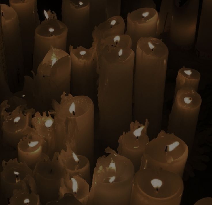 many lit candles are lined up together in a dark room with white lights on them