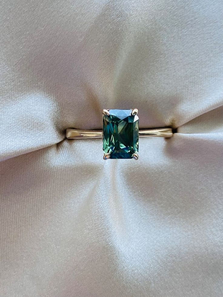 a ring with a green stone on it sitting on top of a white satin material