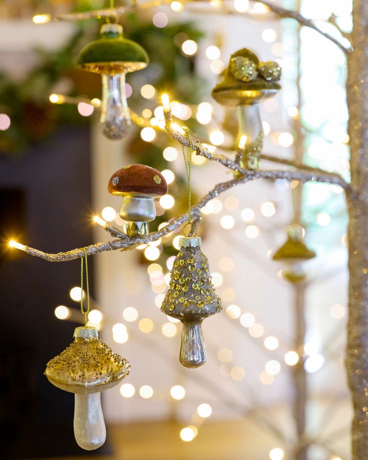 christmas ornaments hanging from a tree with lights in the background