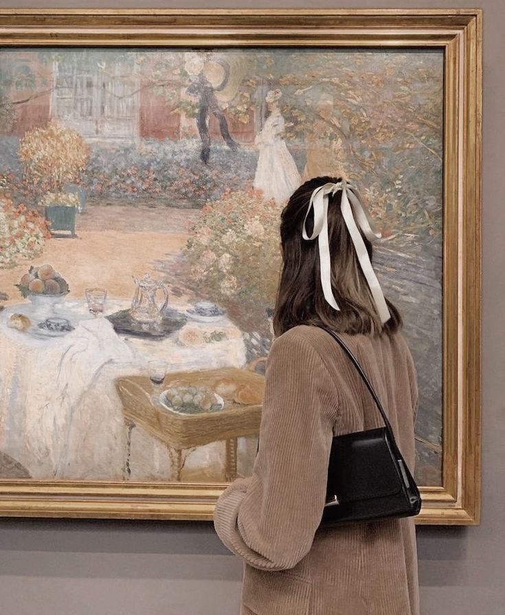 a woman standing in front of a painting with a white bow on her head looking at it