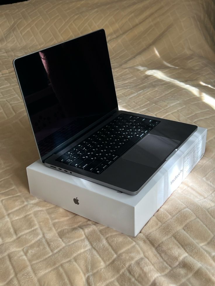 an open laptop computer sitting on top of a white box in the middle of a bed