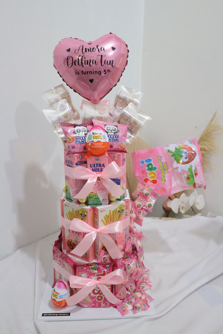 a pink candy tower with a heart shaped balloon in the middle and other candies around it