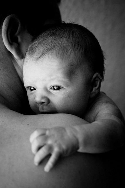 a black and white photo of a baby being held by its mother's arm