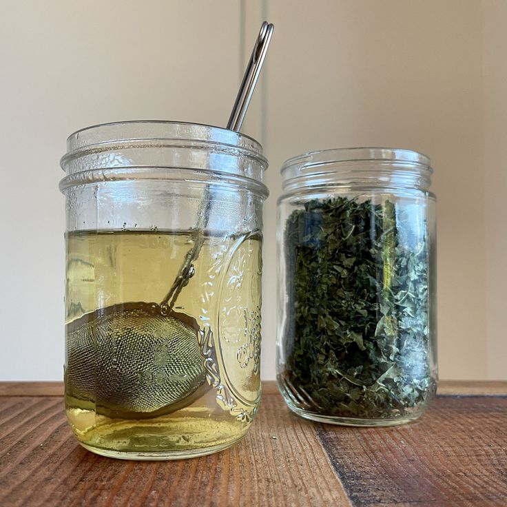 two jars filled with different types of tea on top of a wooden table next to each other