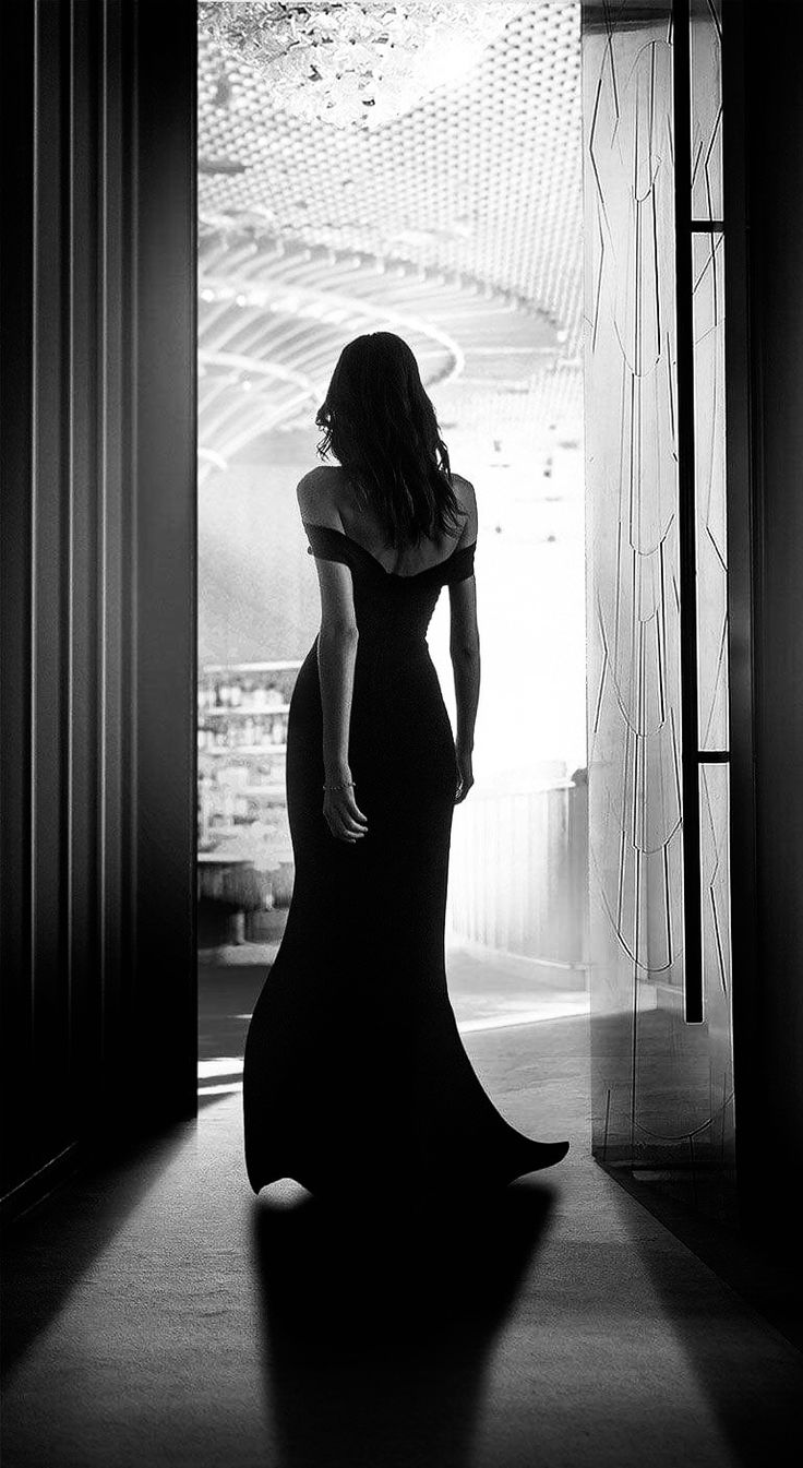 a woman in a long black dress is standing by a door and looking into the room