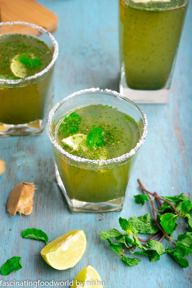 two glasses filled with green drinks and garnished with mint on a blue table