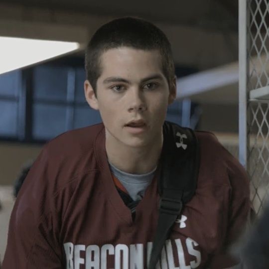 a young man wearing a maroon shirt and carrying a black bag in front of him