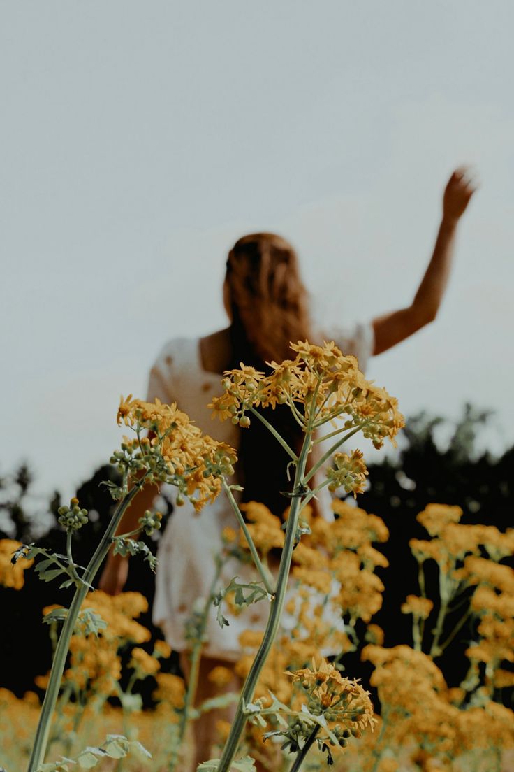 a woman standing in the middle of a field of yellow flowers with her arms outstretched