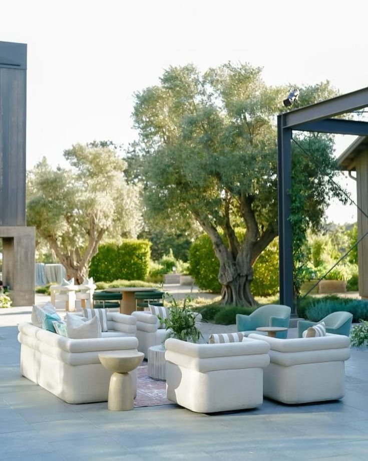 a group of white couches sitting on top of a cement floor next to trees