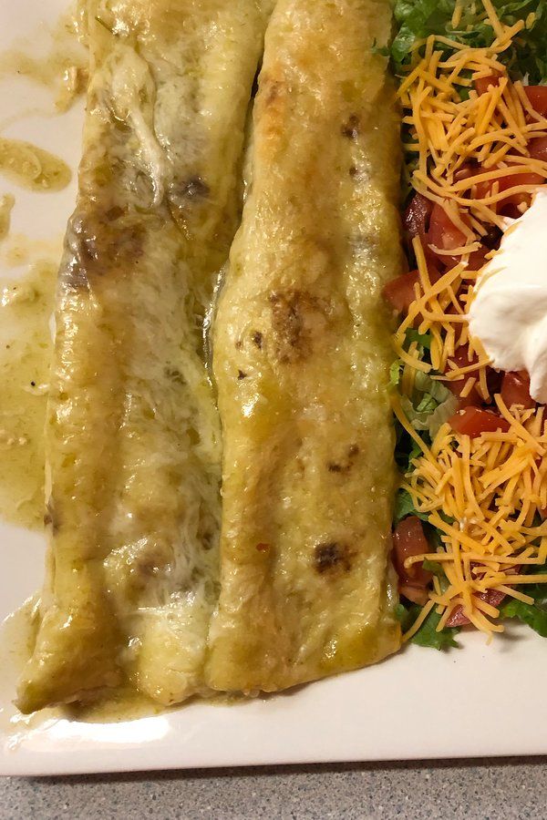 a white plate topped with two enchiladas covered in sauce and cheese next to a salad