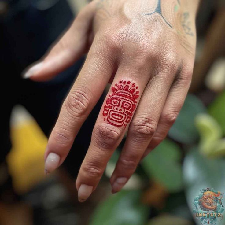 a person with tattoos on their fingers and fingernails is wearing a red ring